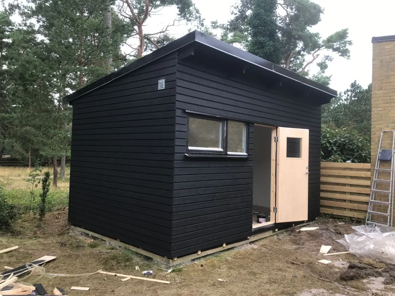 Nybyggt förråd i svartmålad träpanel med fönster och dörr – byggt av Wood & Stone