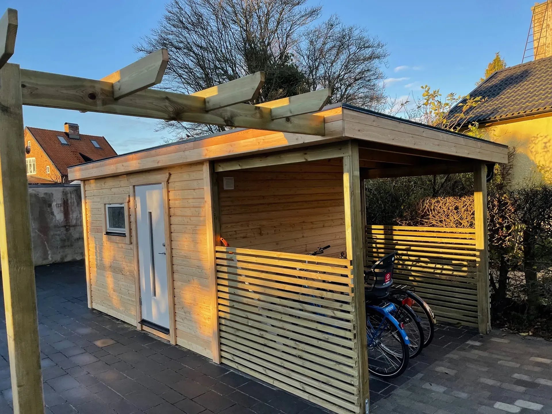 Förråd i trä med ett täckt cykeltak där cyklar står parkerade – byggt av Wood & Stone