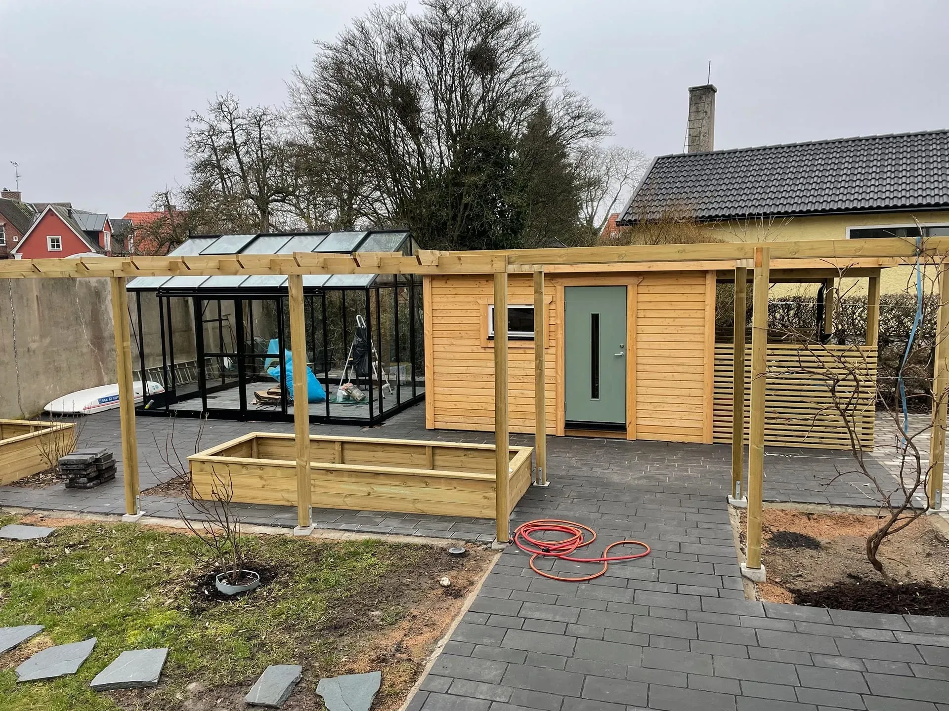 Nytt förråd, pergola, odlingslådor och stenläggning i en trädgård i Lund