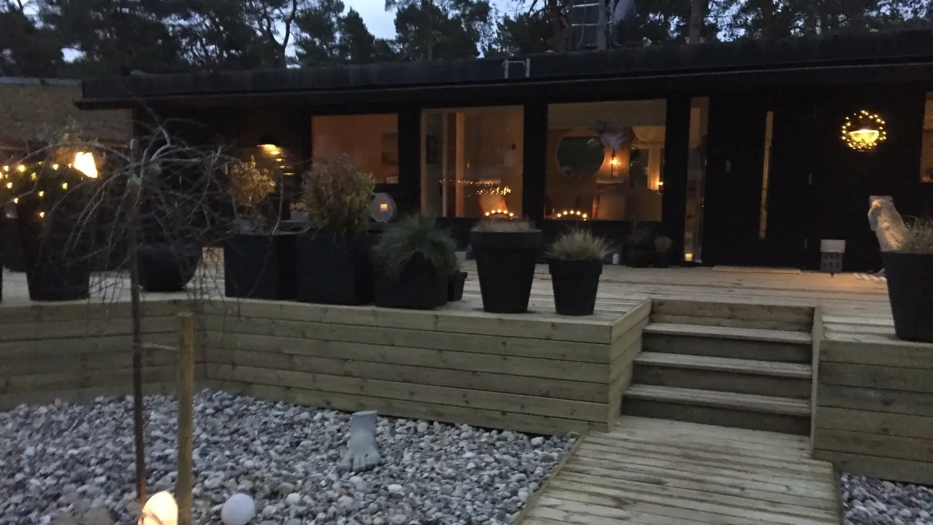 Belyst trädäck och uteplats i skymning, byggd av Wood & Stone